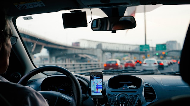 Image of perspective from the backseat of a car showing a person driving in traffic with phone propped up with GPS.