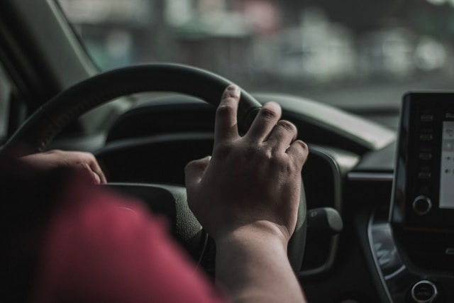 Person in a red shirt with hands on the steering wheel.